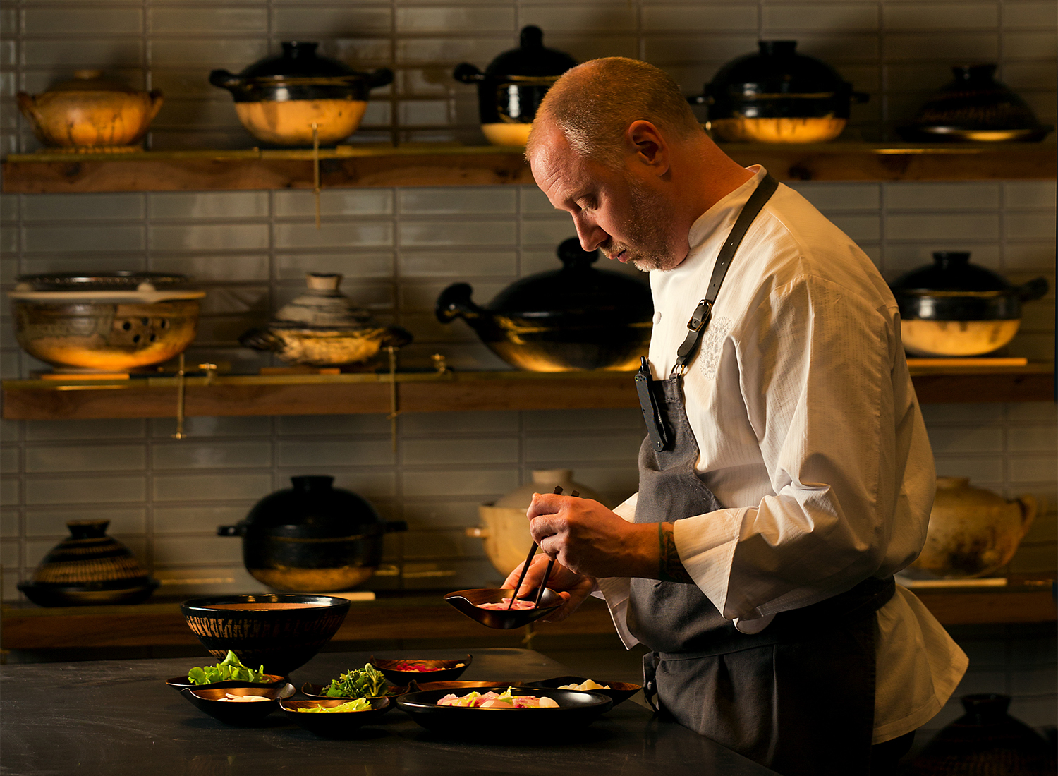 Chef Kyle Connaughton uses a Japanese donabe from his collection, at back on the wall, to cook his Tilefish, Blue Foot, and Chantrelle “Fukkura-San” with Leeks, Brassicas From the Farm, Sansho, and Chamomile Dashi Broth at Single Thread Farms Restaurant in Healdsburg. (John Burgess/The Press Democrat)
