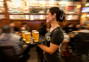 Server Erika Corella carries a tray of Russian River Brewing Co.’s 20th anniversary Pliny the Younger triple IPA for guests on the first day of the limited release at the brewpub in Santa Rosa, Friday, March 22, 2024. (John Burgess / The Press Democrat)